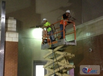 Workers on a scissor lift using pressure washers on a commercial brick exterior wall during professional power washing.