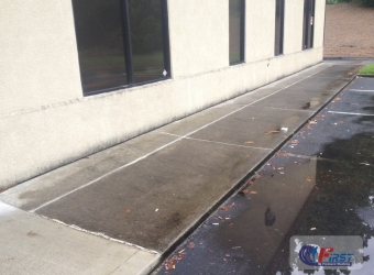Dirty commercial concrete walkway with dark algae stains and standing water before pressure washing